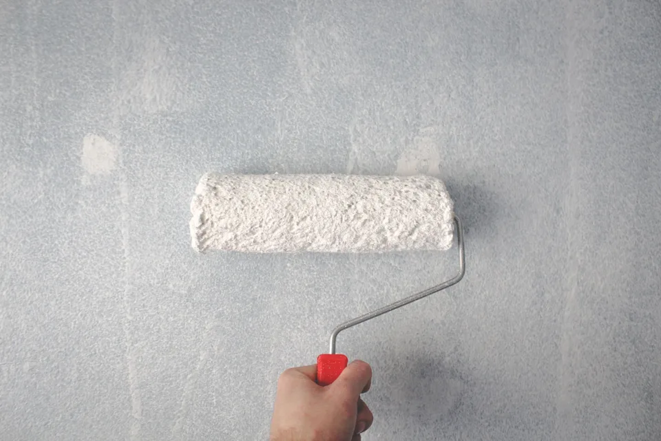 Peintre appliquant une peinture mate sur un mur intérieur blanc dans un salon lumineux et moderne.